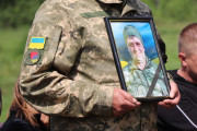  На фотографії зображено військового, що тримає у руках фотопортрет загиблого Захисника Сергія Вікторовича Кривчука. На лівому рукаві форми є нашивка у вигляді прапора України та нашивка тризуба із серцем.