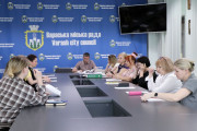 На фотографії, зробленій 24 квітня 2025 року у Вараші, зафіксовано засідання комісії з питань захисту прав дитини. За довгим столом зібралися члени комісії. У центрі столу розміщено документи та канцелярське приладдя. На чолі столу сидить заступник міського голови Роман Хондока у світлій сорочці, який є головуючим. З обох боків від нього розмістилися члени комісії. На задньому плані видно синю стіну з написом українською та англійською мовами: "Вараська міська рада - Varash city council", а також зображення герба міста Вараш. У правому верхньому кутку на стіні висить плаский телевізійний екран. Загальна атмосфера на фото робоча та зосереджена, що підкреслює серйозність обговорюваних питань щодо соціального захисту прав та інтересів дітей у громаді.